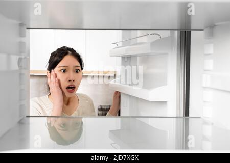 Shocked asian woman looking inside empty fridge Stock Photo