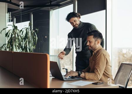Experienced colleague explaining to young coworker business project strategy at contemporary office, copy space Stock Photo