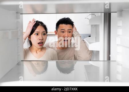 Confused chinese couple looking inside empty fridge at home Stock Photo