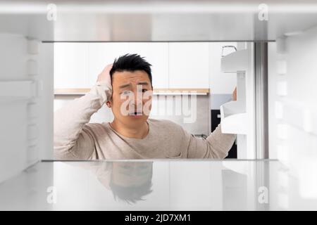 Shocked chinese man looking inside empty fridge Stock Photo
