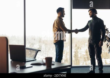 Two serious businessmen shaking hands, making deal or agreement at contemporary office, empty space Stock Photo