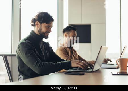 Joyful male coworkers using laptops, working on business project together as team in company office, blank space Stock Photo
