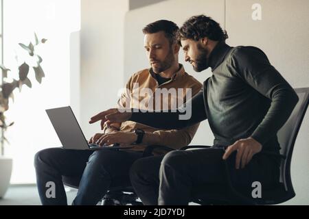Serious male colleagues working together, using laptop computer at contemporary company office, blank space Stock Photo