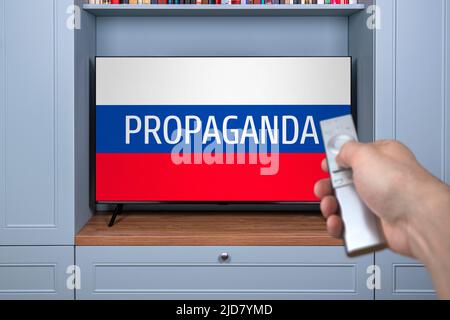 Propaganda TV channels on Russian television. Agitation and russian propaganda in modern television. Misinformation citizen. Remote control in the hand of the guy watching russian news on TV. False TV Stock Photo