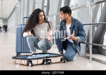 Wrong Suitcase. Confused Arab Couple Sitting Near Open Luggage At Airport Stock Photo