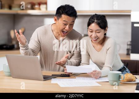 Happy asian couple paying bills online, using computer Stock Photo