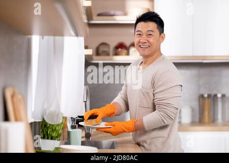 Cheerful chinese man washing dishes at home Stock Photo