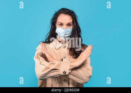 Confident sad young caucasian lady brunette in protective mask show stop sign with crossed hands Stock Photo