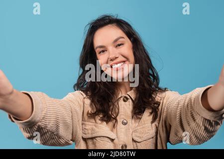 Glad happy young european female brunette student in casual making selfie on device, isolated on blue background Stock Photo