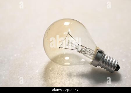 A small incandescent light bulb or lamp on white hard surface Stock Photo