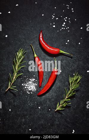 Chilli peppers, rosemary twigs and coarse salt. Flat lay shot of cooking ingredients arranged on dark background. Stock Photo