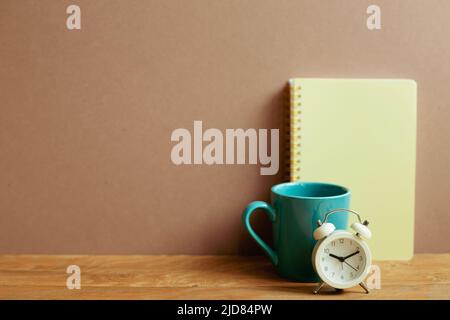 Notebook and mug cup and alarm clock on wooden desk. brown wall background. workspace Stock Photo