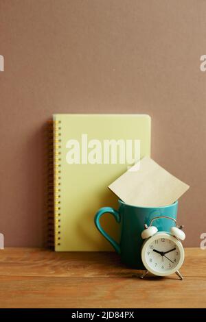 Notebook and mug cup and alarm clock on wooden desk. brown wall background. workspace Stock Photo