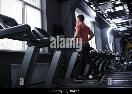Rear view full length shot of a male bodybuilder doing cardio workout, running on treadmill Stock Photo