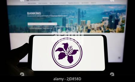 Person holding smartphone with logo of Hong Kong Monetary Authority (HKMA) on screen in front of website. Focus on phone display. Stock Photo