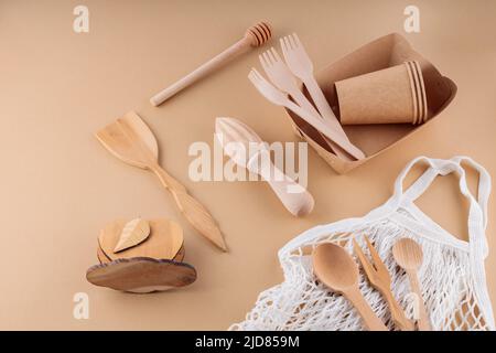 Eco-friendly kitchen utensils, paper disposable tableware and mesh bag. Wooden cutlery and shopping bag on a beige background. Sustainable lifestyle. Stock Photo