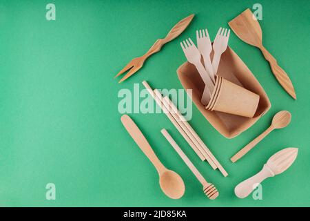 Paper biodegradable tableware and wooden cutlery on a green background. Eco-friendly kitchen utensils, bamboo forks, cardboard containers and cups. Su Stock Photo