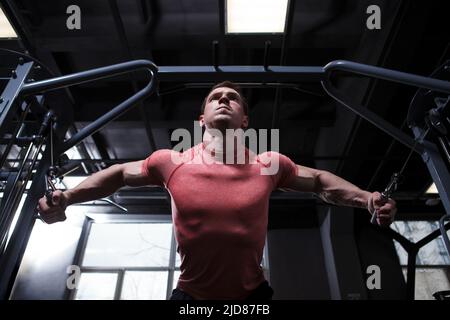 Low angle shot of a muscular bodybuilder working out in cable crossover gym machine Stock Photo