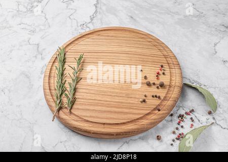 round wooden cutting board with edging. thyme and spices on a white marble background. mockup with copy space for text, side view Stock Photo