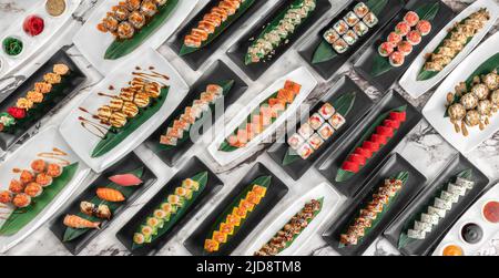 banner with different sets of maki sushi rolls, nigiri and gunkan with tiger shrimp, tomago, salmon, tuna, chuka salad, tuna and bamboo leafs in a whi Stock Photo