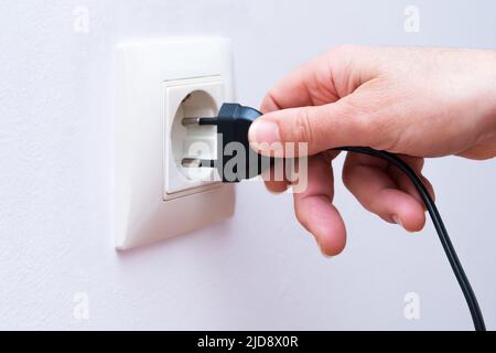 Plugging a black electrical plug into a wall socket with a woman's hand. Stock Photo