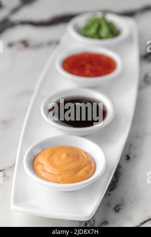 set of sauces for sushi on a white plate, wasabi, spicy, cheesy, soy. bright textured marble background, side view, close-up Stock Photo