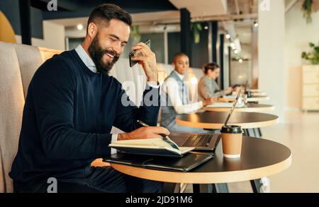 Happy businessman making notes during a phone call. Young businessman smiling cheerfully while making plans with his associates over the phone. Young Stock Photo