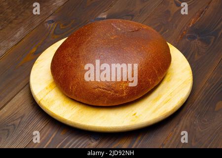 A loaf of black bread. Homemade Baked bread in the oven in one piece. Eco friendly round bread on a white cutting board, against a beautiful brown Stock Photo
