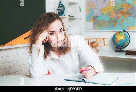 Teenage student. Portrait of a pensive young girl making notes while sitting with books. Stock Photo