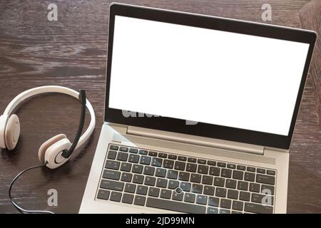 Headset on a laptop, blank white screen, wooden table background, Call center, home office, customer support, help desk, copy space, template. Stock Photo