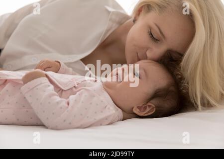 Young loving mother kisses on forehead her lovely baby Stock Photo