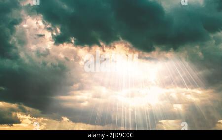 Sun beams shining through dark clouds on sky nature background Stock Photo