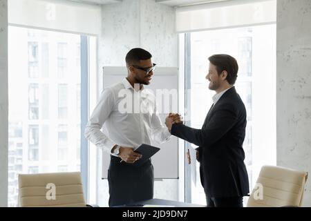 Two millennial multi racial businessmen shake hands express respect Stock Photo