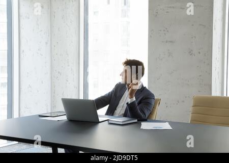 Businessman looks out window at city view seated at workplace Stock Photo