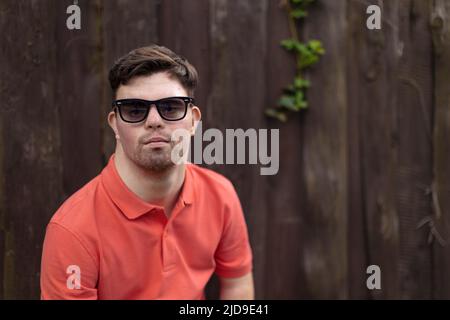 Portrait of happy young man with down syndrome standing outdoors in park and wearing sunglasses Stock Photo
