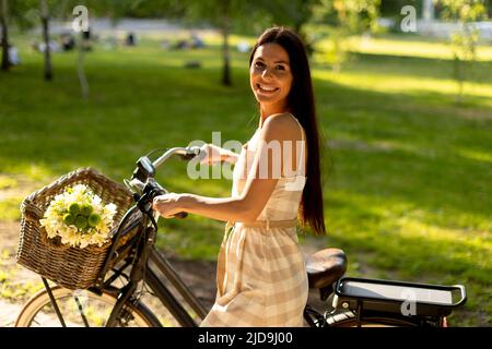 Pretty young woman with flowers in the basket of electric bike Stock Photo