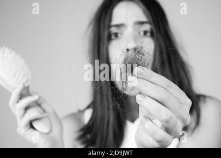 Hair loss in women. Young woman is upset because of hair loss. Portrait of frustrated girl with problem hair, isolated. Worried girl holding long Stock Photo