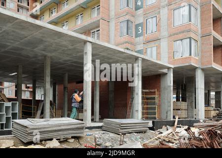 Young female builder in workwear using electric drill while working at construction site in concrete unfinished structure Stock Photo