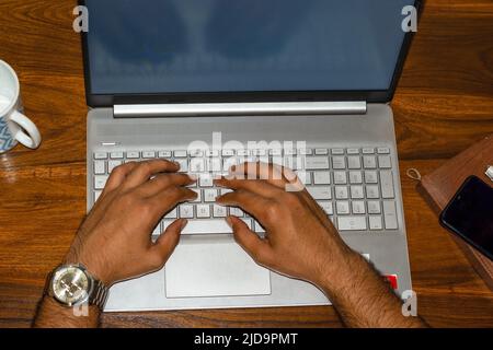 Top view of hands of a man wearing watch typing on laptop. Selective focus on laptop keys. Stock Photo