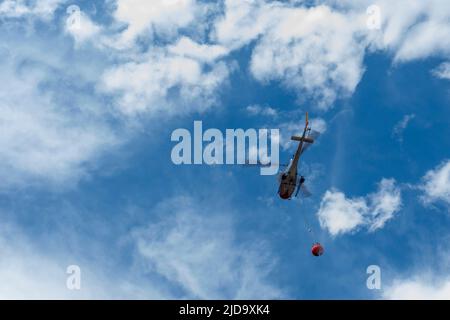 ow angle view of a helicopter with a bucket delivering water to extinguish a fire. Copy space Stock Photo