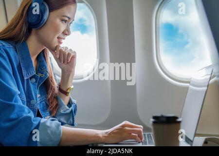 Travel, Portrait of a smiling Asian female tourist while listening to music and using a computer while on the plane Stock Photo