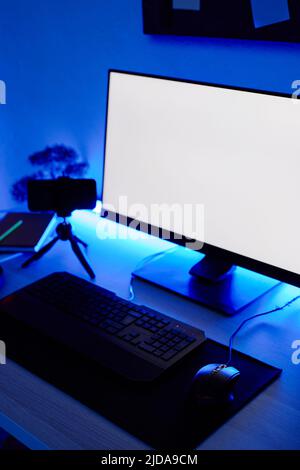 Vertical background image of gaming setup PC on desk lit with blue neon lighting, screen mockup Stock Photo