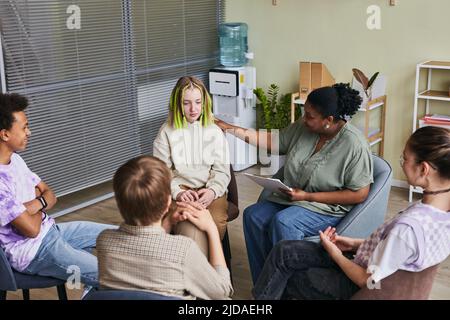 Group of teenagers sitting on chairs and talking their problems to psychologist who listening to them and giving advice during psychology therapy grou Stock Photo