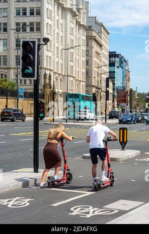 Young man and woman riding Voi E-scooters setting off on a green light at a traffic light controlled bike lane, Liverpool, England, UK Stock Photo