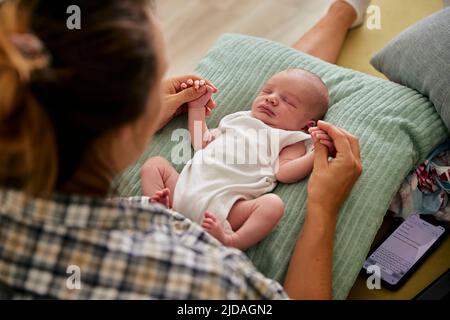 Mother holding hands of sleeping three month old baby boy lying on his back. Stock Photo