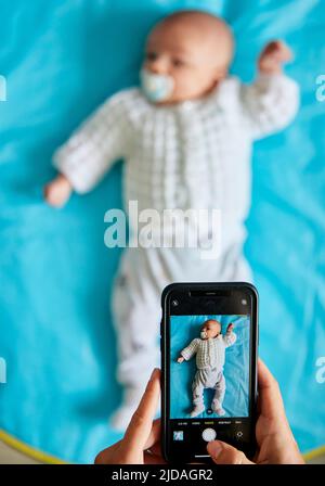 Parent taking photograph of baby lying down using smart phone, shot from above