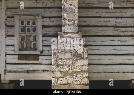 An abandoned log cabin  with a stone chimney flue, cracked and dried out wood cladding and broken window.