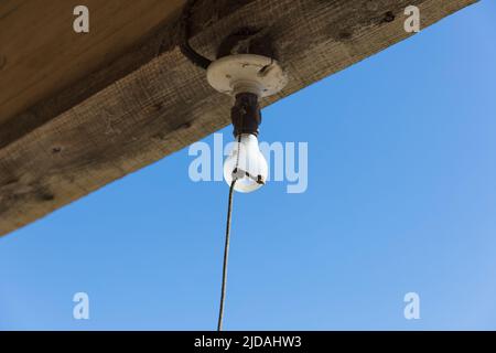 Old incandescent light bulb on a porch beam with a string pull control.