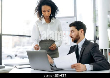 Successful multiracial business colleagues, african american woman and caucasian man, working in a modern office, looking through documents, working on a joint project to modernize the workflow Stock Photo