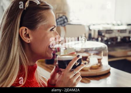 Young beautiful woman in red sweeter sitting at a cafe having morning coffee near the bar, Visitor ordering morning drink  Stock Photo